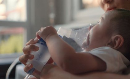 Child lying on bed with nebuliser mask on face.